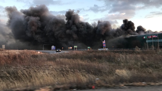 A large industrial building is seen covered in black smoke near Hwy. 403/QEW and Appleby Line in Burlington. (Twitter/@RockoGta)
